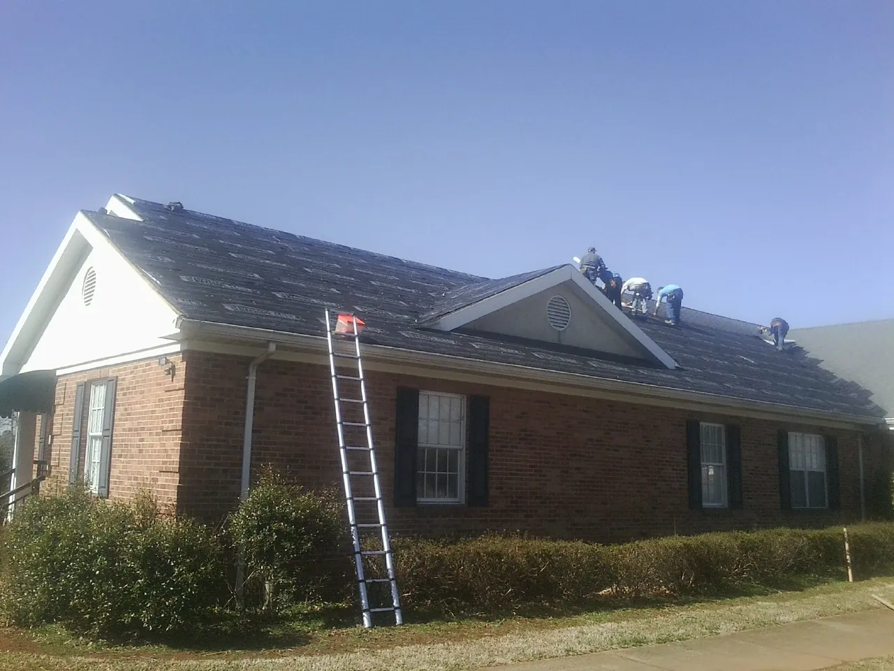 Crew tearing shingles off a brick ranch roof with a ladder set — Metal Roof Repair work by our crew in Collinsville