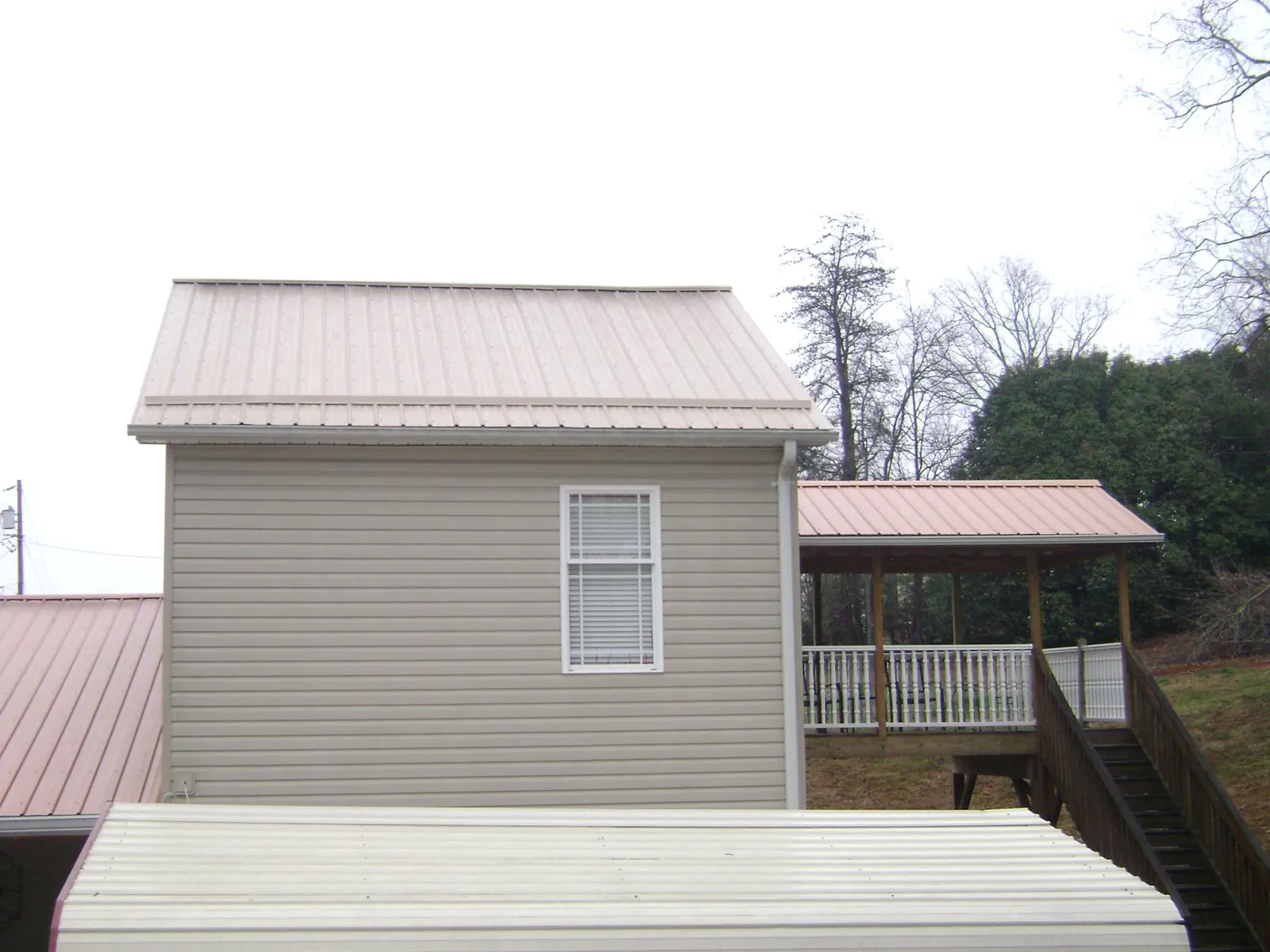 Tan metal roofs on a two story addition and attached porch, from a Roof Replacement job in Collinsville